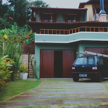 Sobrado com fachada verde-água e portão de garagem em madeira escura